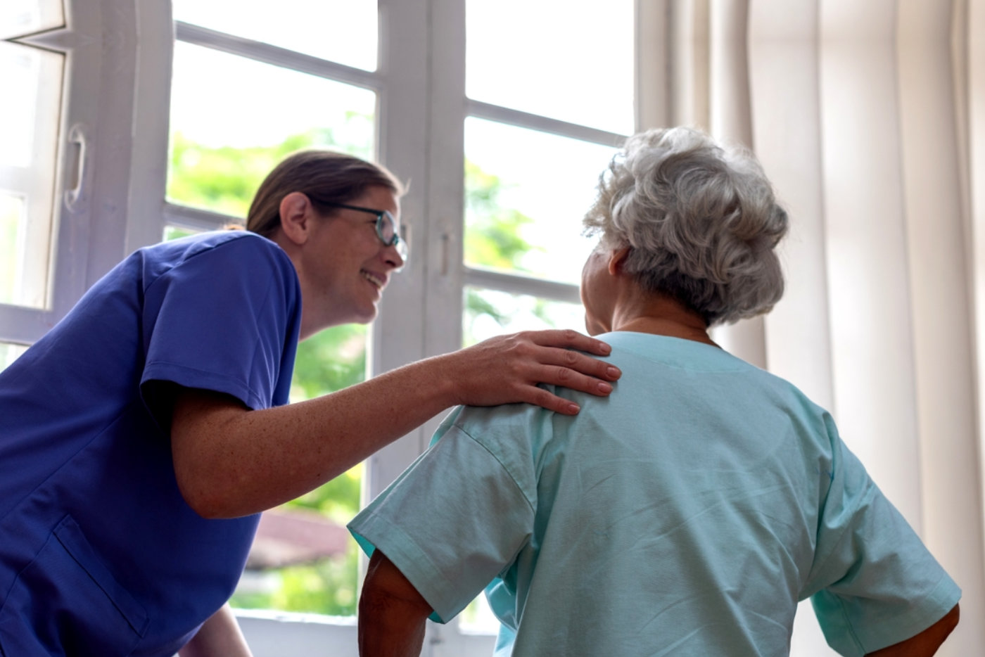 Caregiver supports elderly woman indoors.